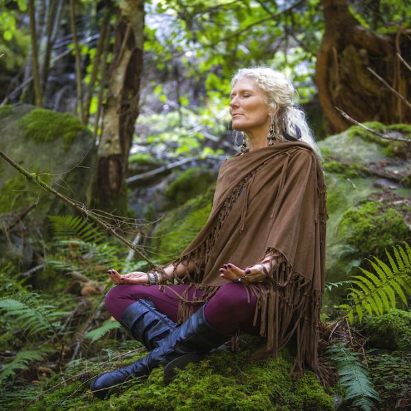 Charlotte Saint Jean fait une méditation pour se connecter à la Terre, seule, assise en tailleur sur une rocher, en pleine nature, dans la forêt.